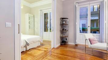 Une chambre d’hôtel avec un plancher en bois, un lit, une chaise, une étagère et une porte donnant sur un balcon.