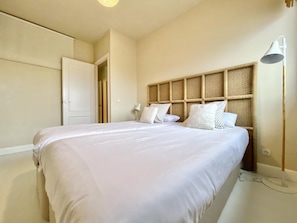 A bedroom with a large bed, a headboard with a woven design, a bedside lamp, and a wardrobe.