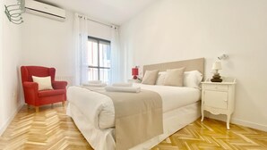 A hotel room with a large bed, a red armchair, a bedside table with a lamp, and a window with curtains. - Charming Gran Vía V - in the City Center (Madrid)