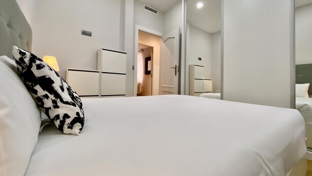 A modern hotel room with a large bed, a wardrobe, a mirror, and a door leading to another room. - Charming Atocha - Temporary stays (Madrid)