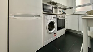 A compact kitchen with a refrigerator, washing machine, oven, and microwave. - Charming Atocha - Temporary stays (Madrid)
