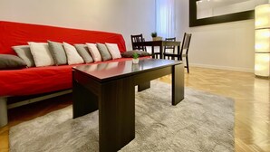 A modern living room with a red sofa, a dark wooden coffee table, and a dining area with a table and chairs. - Charming Atocha - Temporary stays (Madrid)