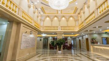 Um hall imponente com lustre, piso de mármore e balcão de recepção.