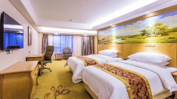 A hotel room with two beds, a desk, a chair, a television, and a painting on the wall. - Vienna International Hotel (Shanghai)