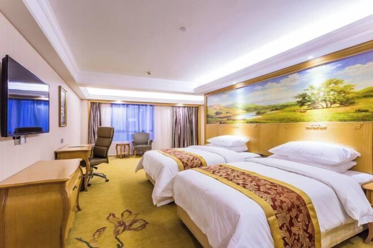 Una habitación de hotel con dos camas, un escritorio, una silla, un televisor y un cuadro en la pared.