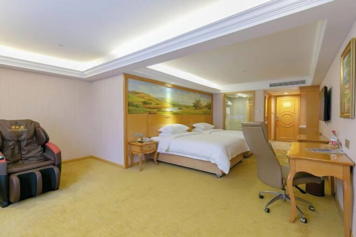 Habitación de hotel con cama, sillón de masaje, escritorio y un cuadro en la pared.