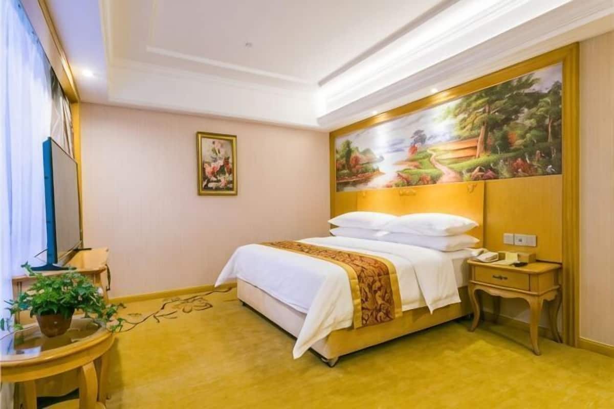 Una habitación de hotel con cama, mesita de noche, lámpara y un cuadro en la pared.