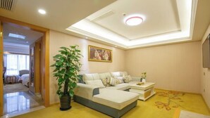 A modern living room with a sectional sofa, a potted plant, and a flat-screen TV mounted on the wall. - Vienna International Hotel (Shanghai)