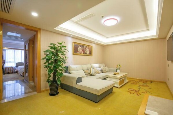 A modern living room with a sectional sofa, a potted plant, and a flat-screen TV mounted on the wall. - Vienna International Hotel (Shanghai)