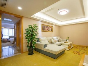 A hotel room with a sofa, a coffee table, a plant, and a painting on the wall. - Vienna International Hotel (Shanghai)