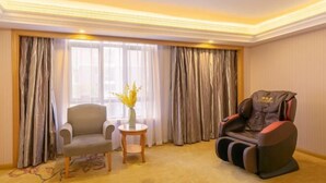 A room with a massage chair, a small table with a vase, and a chair by a window with curtains. - Vienna International Hotel (Shanghai)