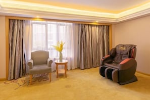 A room with a massage chair, a small table with a vase, and a chair by a window with curtains. - Vienna International Hotel (Shanghai)