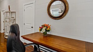 Une pièce avec un bureau en bois, une chaise, une porte blanche et un miroir au mur.
