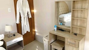 Ein Hotelzimmer mit einem Holzschrank, einem Nachttisch mit Lampe, einem Spiegel und einem kleinen Hocker.
