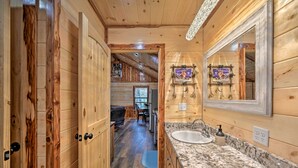 A wooden interior with a bathroom featuring a sink and mirror, wooden walls, and a ceiling with exposed beams. - Cozy Broken Bow Cabin, Walk to the Lukfata Creek! (Broken Bow)