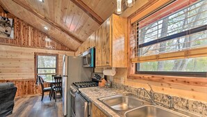 A wooden cabin interior with a kitchen area featuring granite countertops, stainless steel appliances, and a large window with blinds. - Cozy Broken Bow Cabin, Walk to the Lukfata Creek! (Broken Bow)