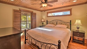 A bedroom with a bed, a nightstand, a desk, a ceiling fan, and a window.