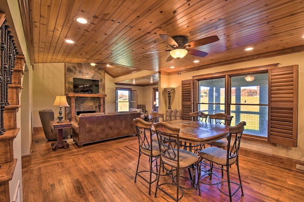 A spacious living room with a wooden ceiling, a fireplace, a television, and a dining area with a large table and chairs.