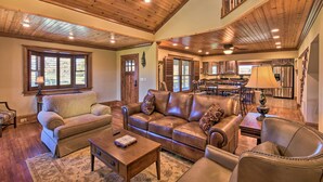 A spacious living room with a wooden ceiling, leather sofas, a coffee table, and a dining area with a chandelier.