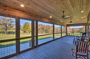 A covered outdoor deck with wooden flooring, large windows, and a view of a golf course.
