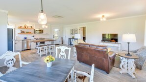 A spacious living area with a dining table, a brown leather sofa, and a television in the background. - Modern Clarkesville Cottage w/ Decks & Patio! (Clarkesville)