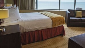 Ett hotellrum med en stor säng, ett nattduksbord, en lampa, en soffa och utsikt över havet.