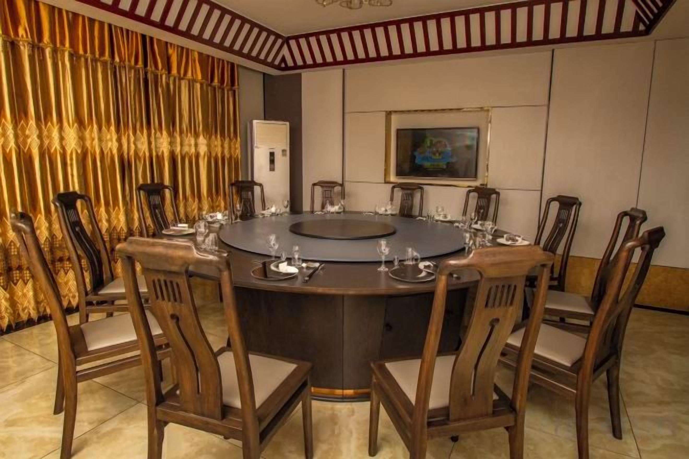 A round table with chairs, a painting on the wall, and a curtain with a pattern.