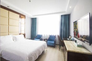 A hotel room with a large bed, two armchairs, a small table, and a desk with a chair. There is a painting on the wall and a window with curtains. - Lingzhou International Hotel (Fang County)