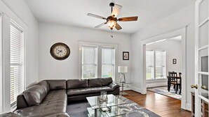A living room with a leather sofa, a glass coffee table, a ceiling fan, and a large wall clock. - The Urchin - Quick stroll to the beach!!! (Galveston)