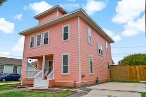 Une maison rose à deux étages, dotée d’un porche à l’avant et d’une clôture en bois.