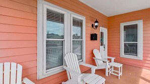 A porch with white Adirondack chairs and a small table, orange siding, and a black mailbox. - The Urchin - Quick stroll to the beach!!! (Galveston)