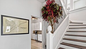 A staircase with white railings and dark steps, leading to a kitchen area with white cabinets and a tiled floor. - The Urchin - Quick stroll to the beach!!! (Galveston)