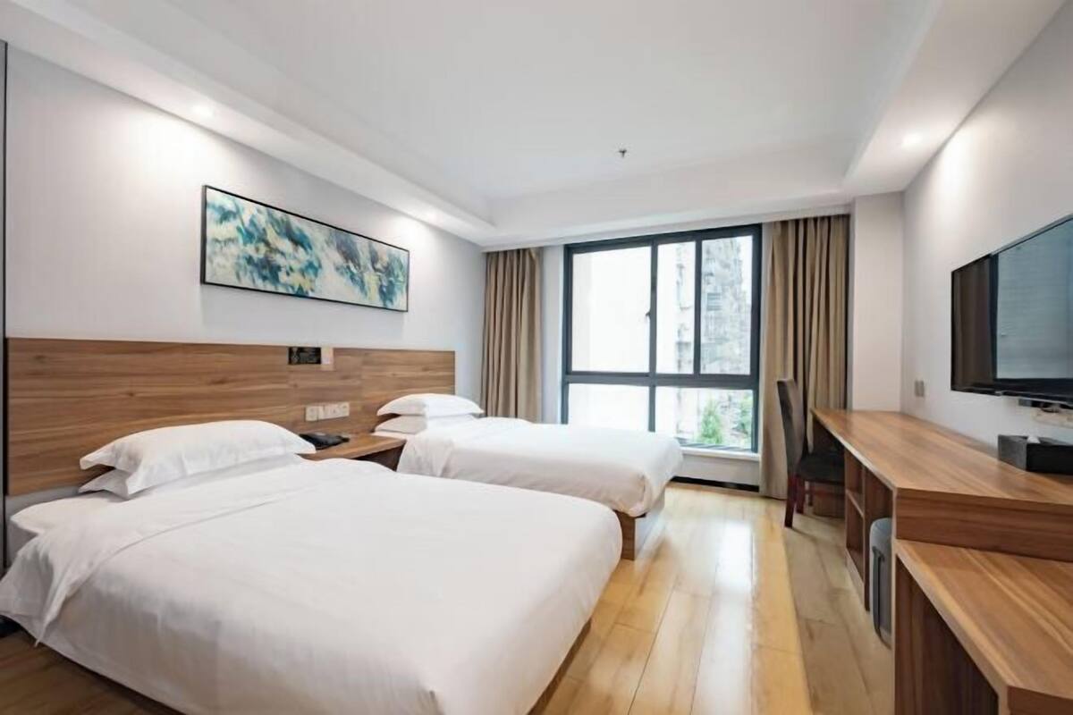 Habitación de hotel con dos camas, un escritorio de madera, un televisor y un ventanal con cortinas.