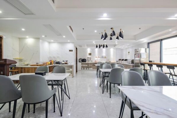Un comedor moderno con mesas y sillas, una cocina al fondo y vistas por la ventana.