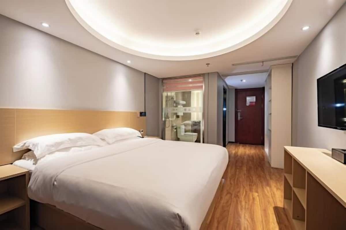 Habitación de hotel con una cama grande, televisión, escritorio y baño visible a través de un mamparo de vidrio.
