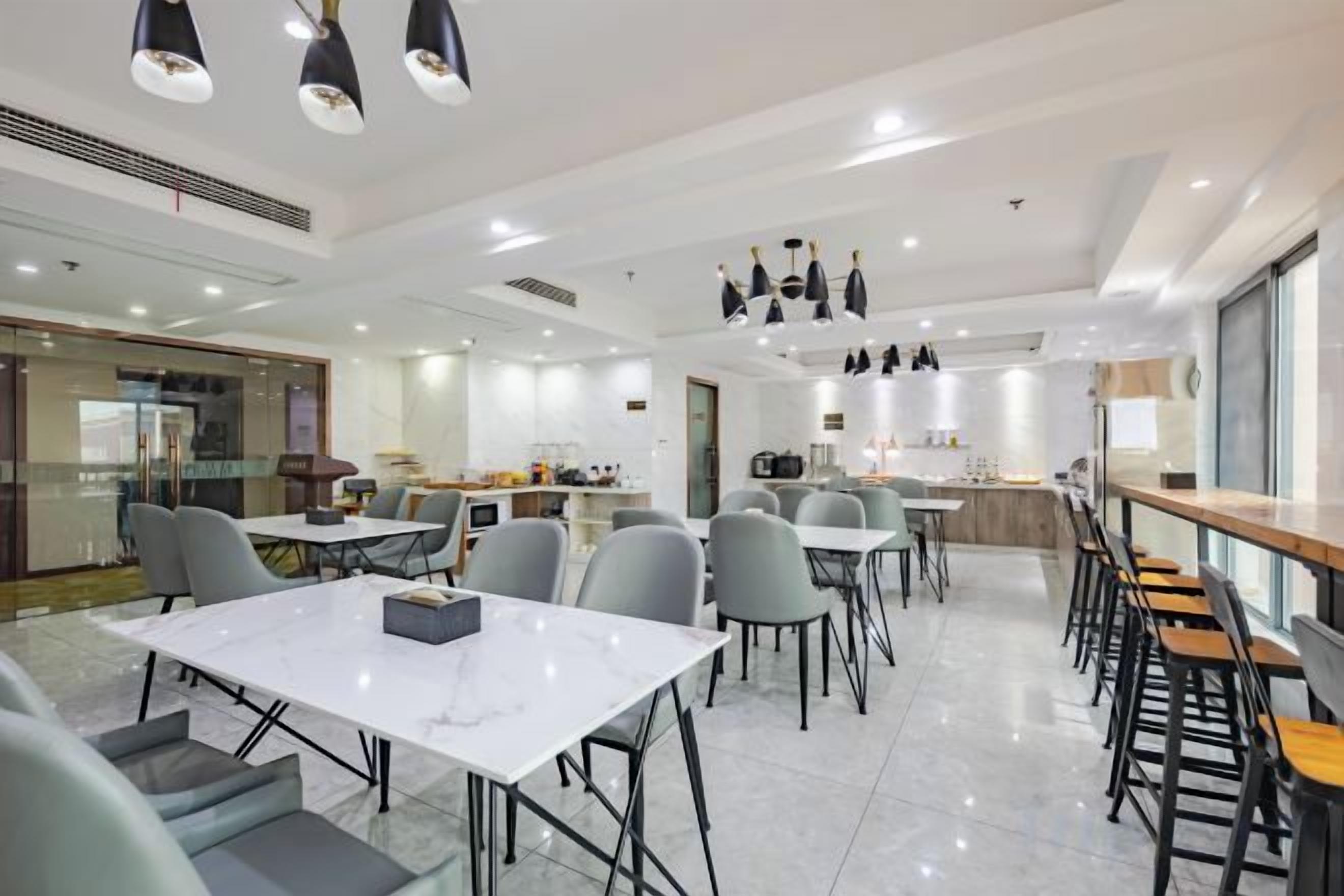 A modern dining area with tables and chairs, a kitchen in the background, and pendant lighting.