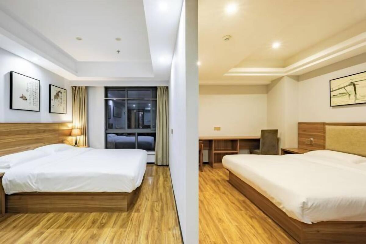 Habitación de hotel con dos camas, suelo de madera, un escritorio y una ventana con cortinas.
