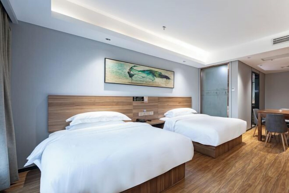 Habitación de hotel con dos camas, cabecera de madera, un cuadro en la pared y un escritorio con sillas.