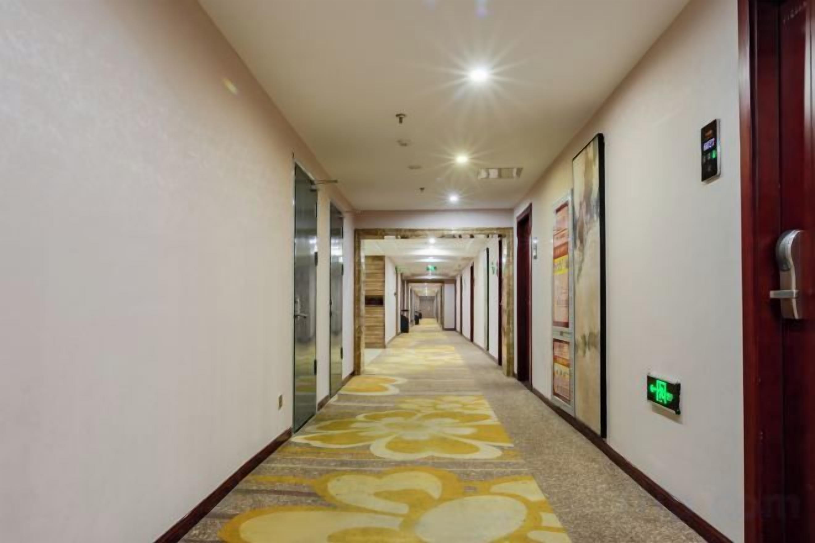 A hotel corridor with a patterned carpet, doors on both sides, and a green exit sign.