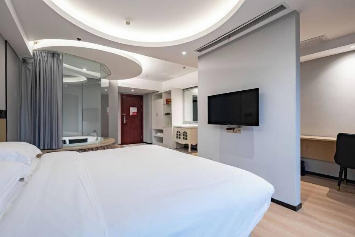 Una habitación de hotel moderna con una cama grande, un televisor de pantalla plana, un escritorio y un baño con cabina de ducha de vidrio.