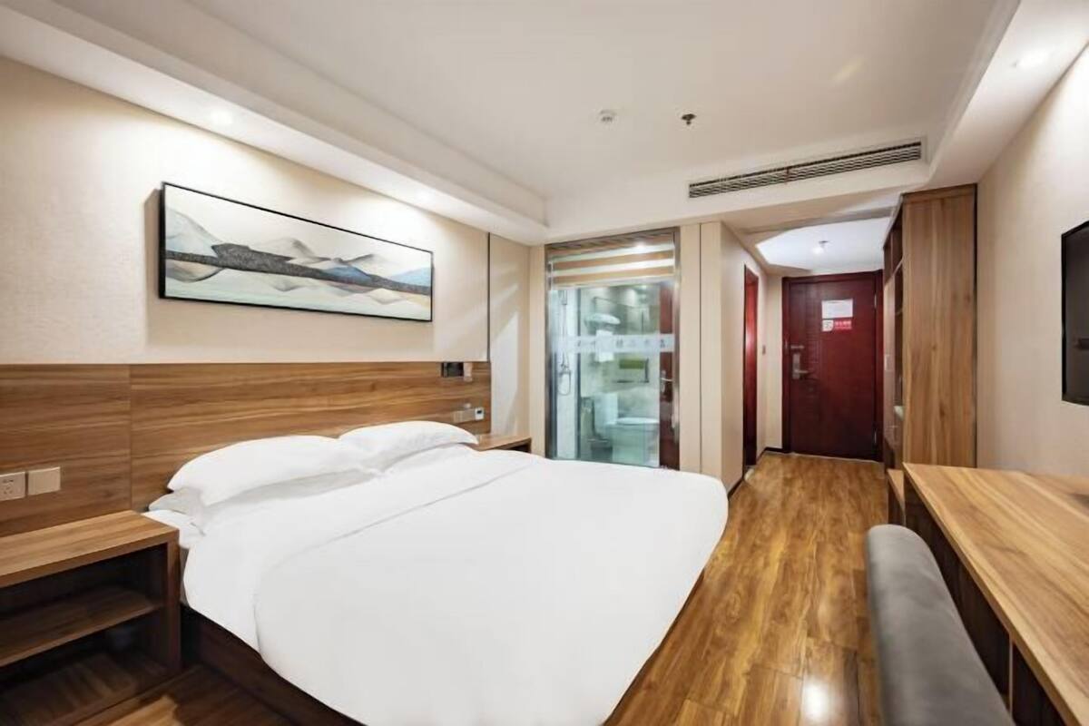 Habitación de hotel con cabecera de madera, una cama grande, una banca, un escritorio y un televisor.