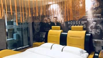 Une chambre d’hôtel avec un lit, deux têtes de lit tapissées de jaune et de noir, une paroi de douche en verre et une affiche accrochée au mur.