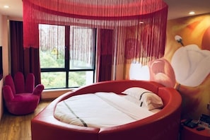 Een moderne slaapkamer met een rond bed, een rode stoel en een groot raam met gordijnen.