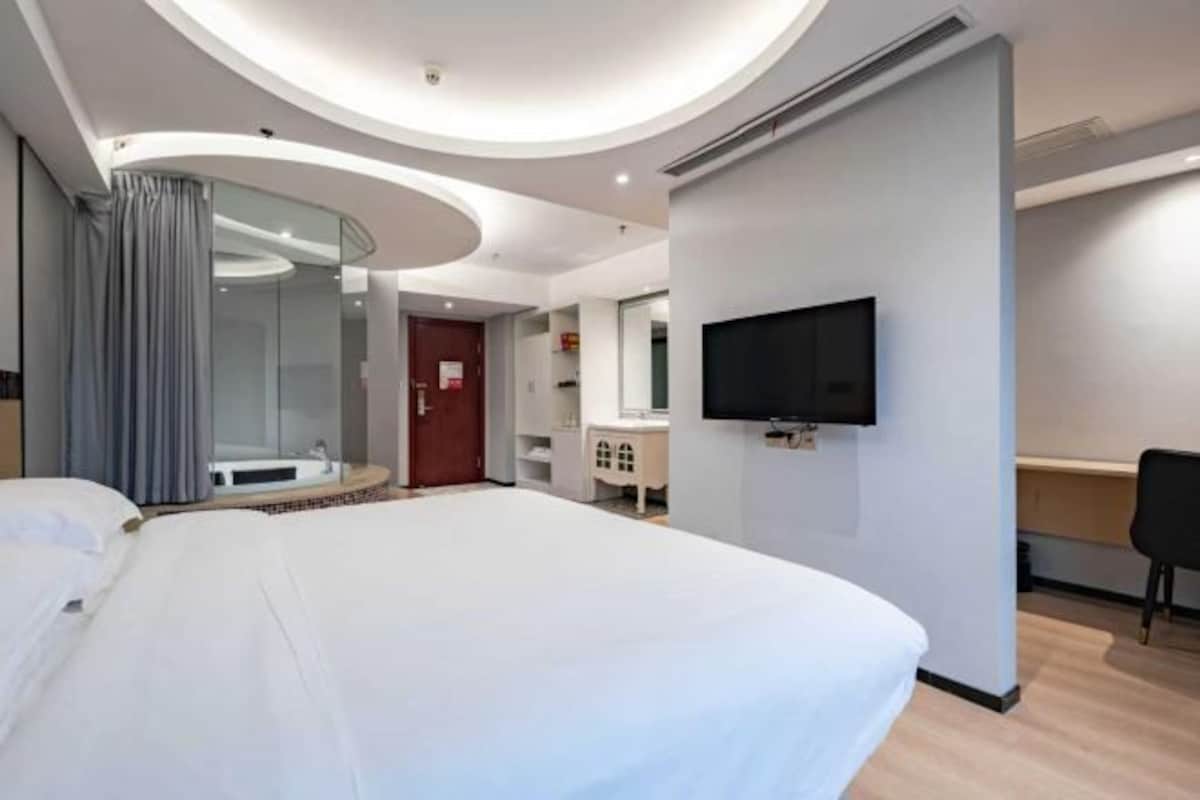 Een moderne hotelkamer met een groot bed, een aan de muur bevestigde televisie, een badkamer met een douchecabine van glas en een bureau.