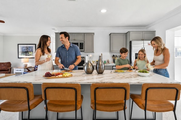 A modern kitchen with a central island, grey cabinets, and a marble countertop.