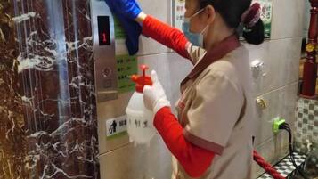 A person cleaning a marble elevator with a spray bottle and a cloth.