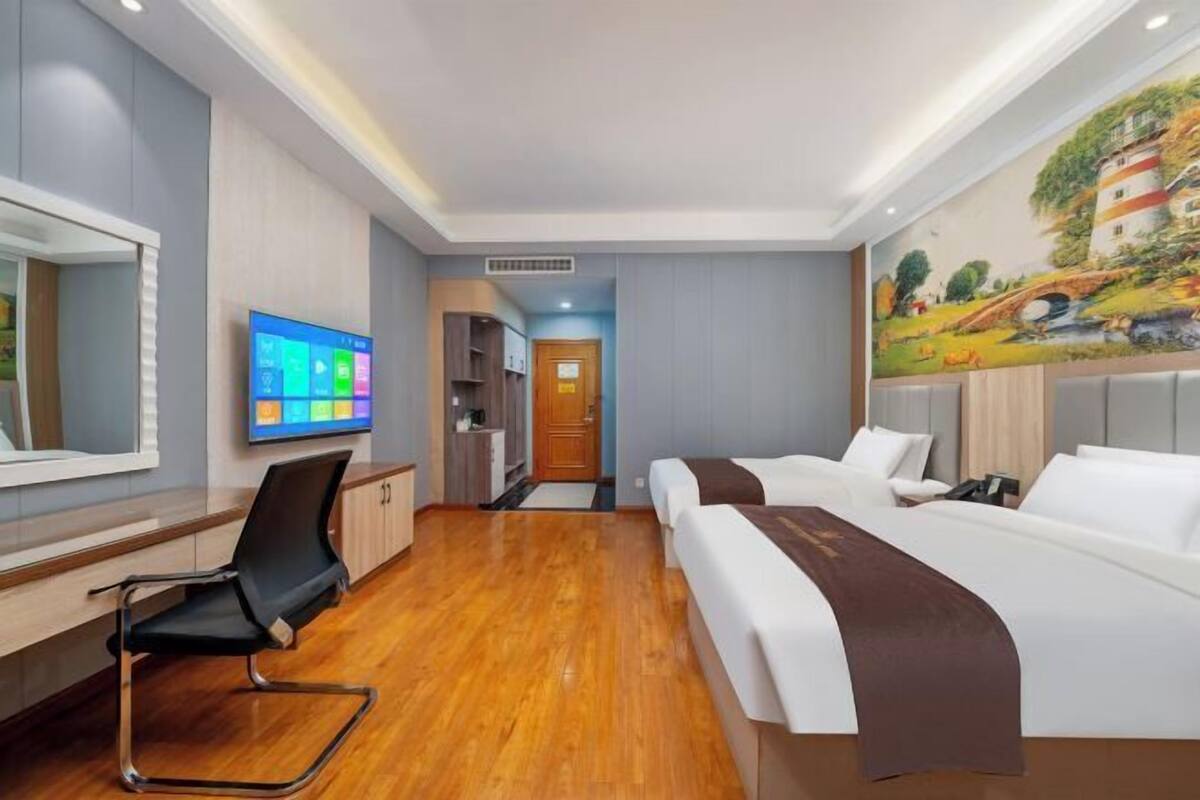 Ein Hotelzimmer mit einem großen Bett, einem Schreibtisch mit Stuhl, einem Wandfernseher und einem Wandgemälde.
