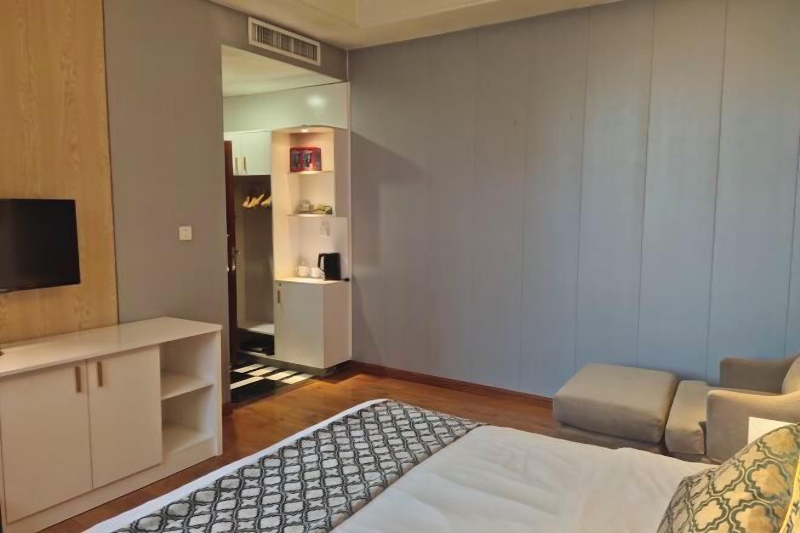 A hotel room with a bed, a TV, a wardrobe, a desk, and a small seating area.