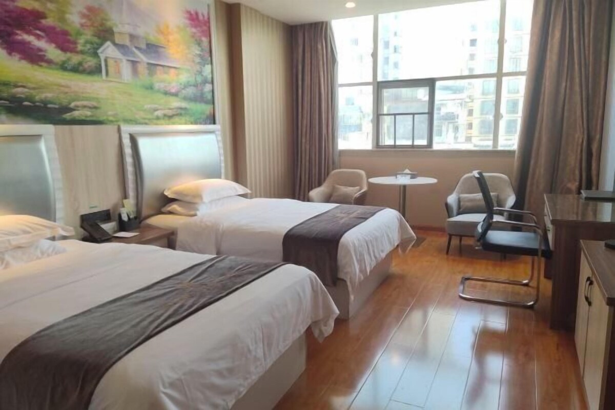 Une chambre d’hôtel avec deux lits, un bureau, une chaise et une fenêtre donnant sur des immeubles.