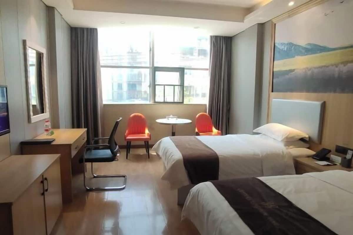 Ein Hotelzimmer mit zwei Betten, einem Schreibtisch mit Stuhl, einem kleinen Tisch und einem Fenster mit Vorhängen.